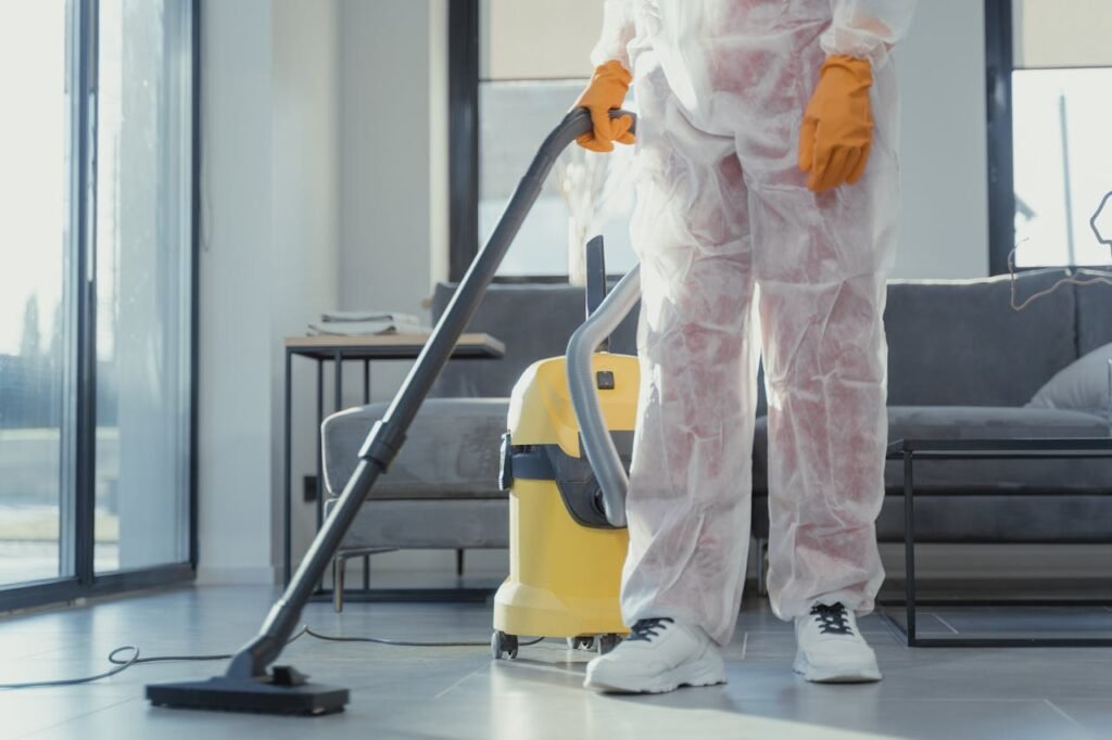 pexels-photo-6195951 A cleaner in protective coveralls and gloves vacuuming a modern living room.